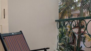 Ein Balkon mit einem Streifenstuhl, einem Metallgeländer und Blick auf eine Palme sowie Gebäude.