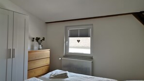 A bedroom with a bed, a dresser, a radiator, and a window with blinds. - Holiday Apartment Neukalen for 4 Guests (Neukalen)