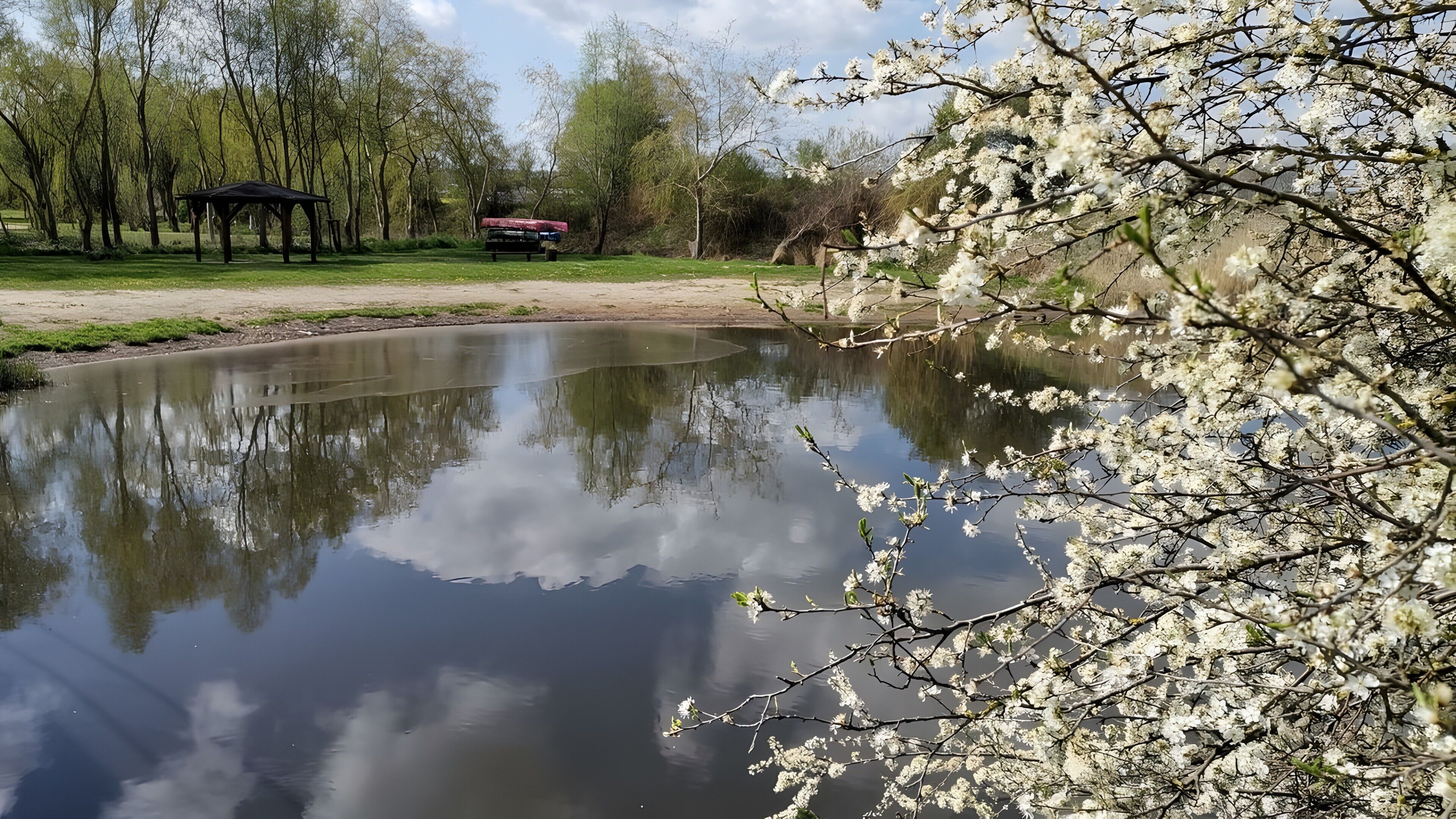 Un étang aux reflets paisibles, bordé d’arbres et agrémenté d’un belvédère.