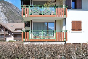 Un bĂątiment Ă deux Ă©tages dotĂ© dâun balcon, dâune fenĂȘtre avec un rideau et, en arriĂšre-plan, dâune montagne.
