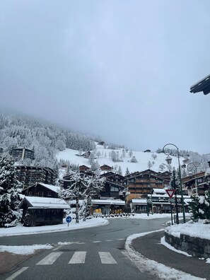 A snow-covered village with wooden buildings, a ski rental sign, and a pedestrian crossing. - Spacious Apartment for 6 – Lake, Ski-in/Ski-out, Balcony & Wi-Fi (Thônes)