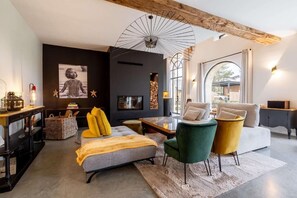 A modern living room with a sofa, chairs, a coffee table, and a fireplace. There is a large window providing natural light and a view outside. - Les Granges de Juvardeil (Juvardeil)