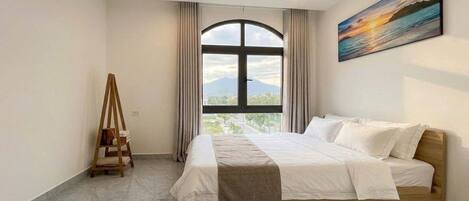 A hotel room with a bed, a window, a painting, and a wooden ladder.