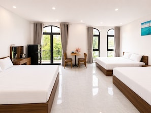 Une chambre d’hôtel avec deux lits, un bureau avec une chaise, une petite table avec un vase et de grandes fenêtres avec des rideaux.