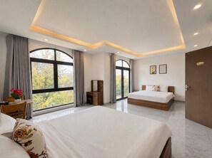 Hotelkamer met een groot bed, een bureau, een stoel en een raam met uitzicht op bomen.
