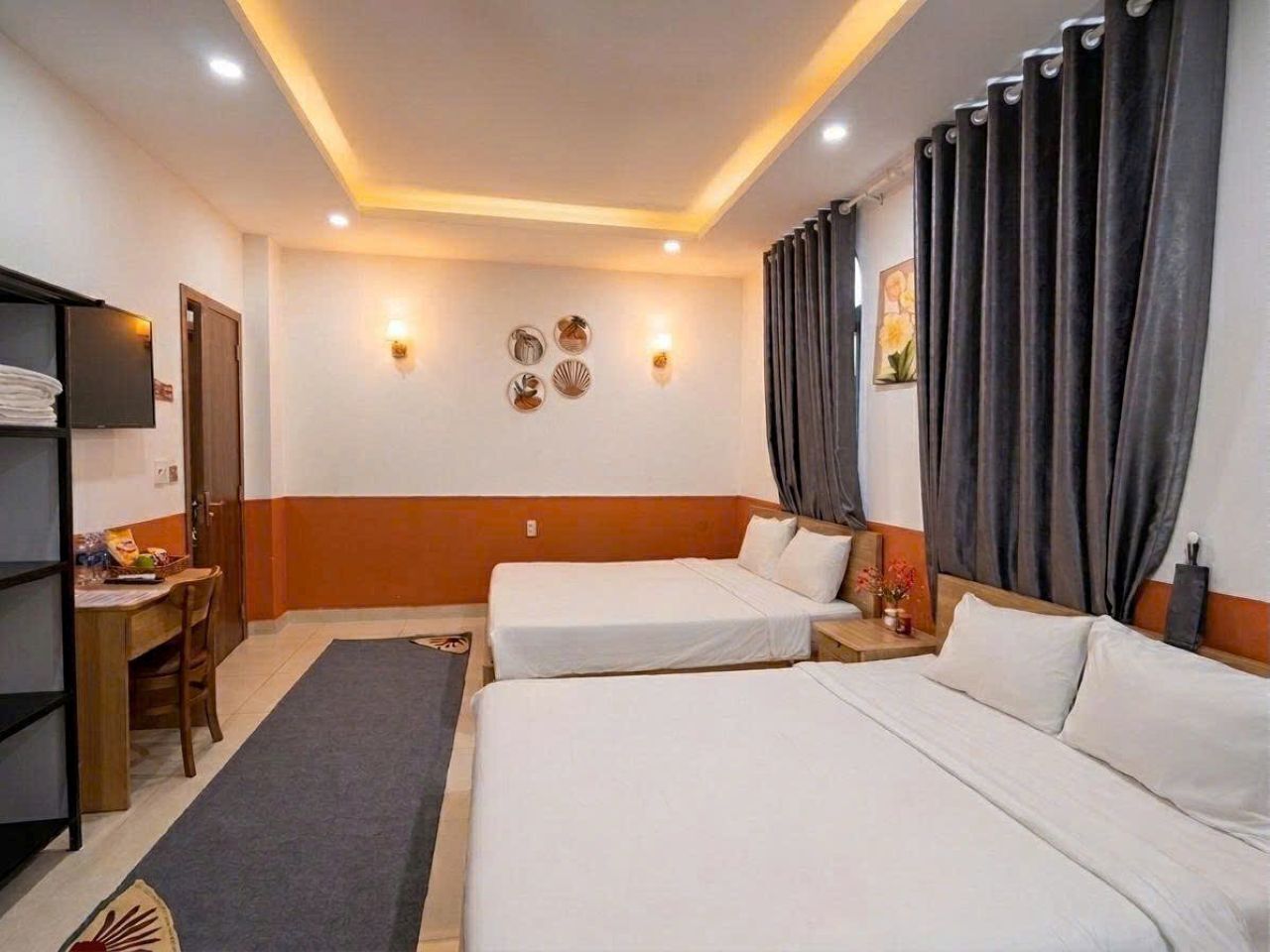 A hotel room with two beds, a desk, and a shelf.