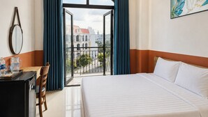 A hotel room with a bed, a desk with a chair, a mirror, and a view of buildings through a balcony. - Dumi Havana Homestay Grand World Phu Quoc (Phu Quoc)