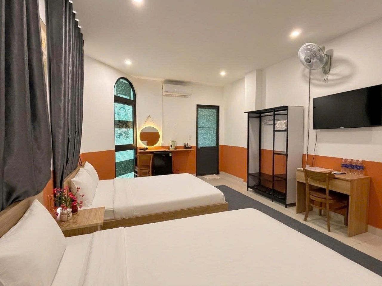 A hotel room with two beds, a desk, a chair, a TV mounted on the wall, and a wardrobe.