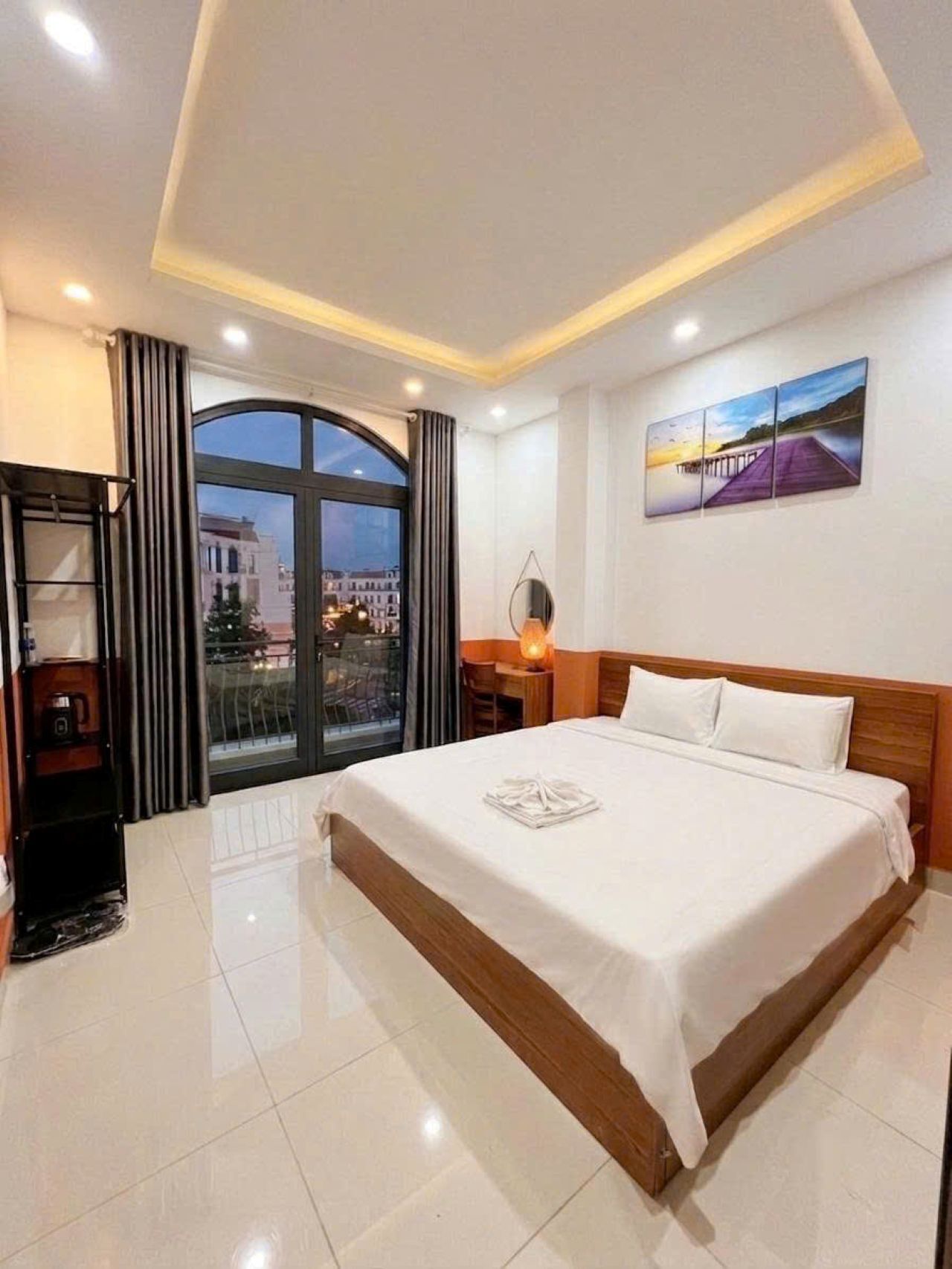 Habitación de hotel con una cama grande, un escritorio, una silla, un ventanal con cortinas y un cuadro en la pared.