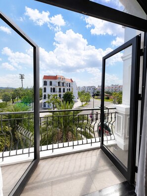 Een balkon met uitzicht op een wit gebouw met een rood dak, omgeven door groen en een heldere lucht.