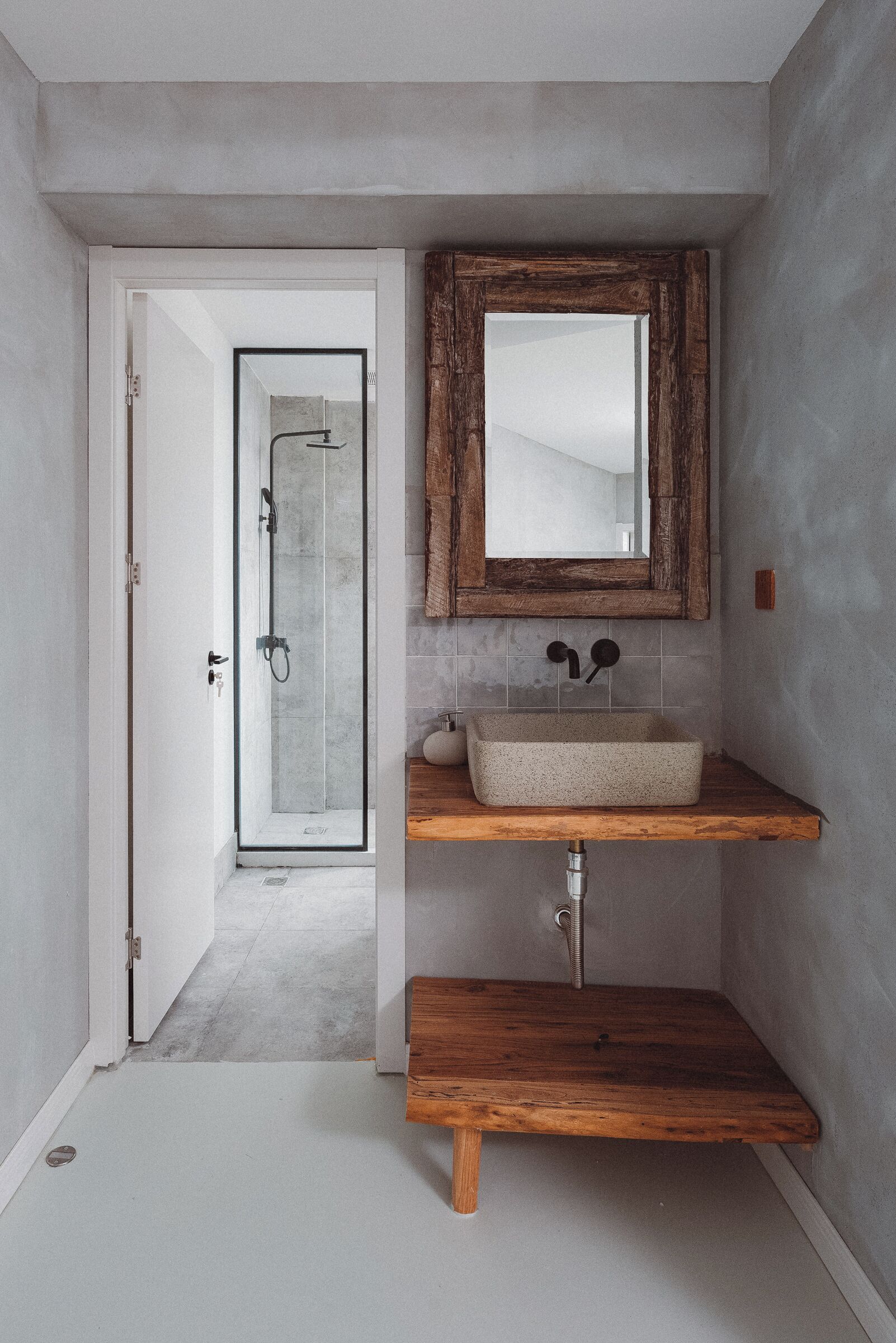 A bathroom with a glass shower door, a wooden shelf, and a mirror with a rustic frame.