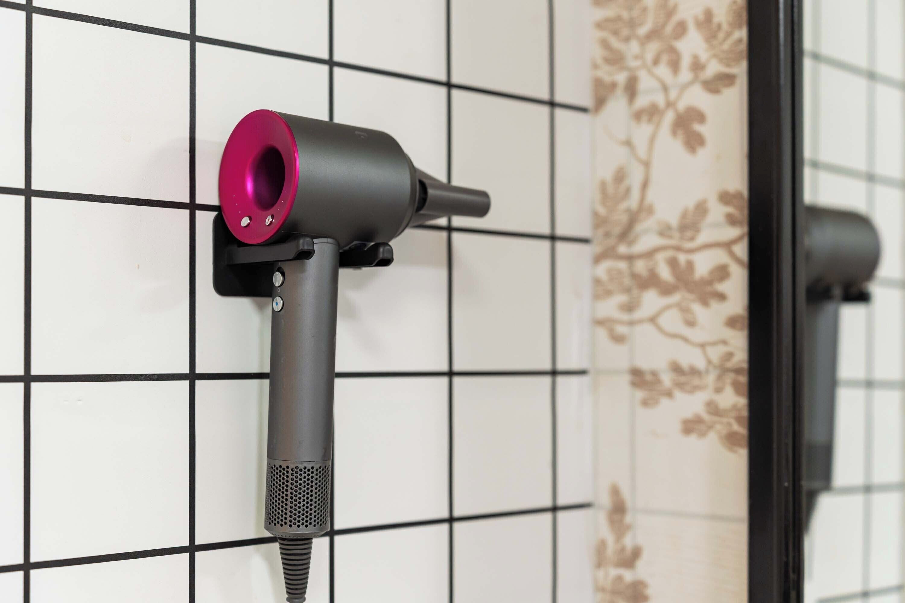 A hairdryer mounted on a tiled wall with a floral pattern.
