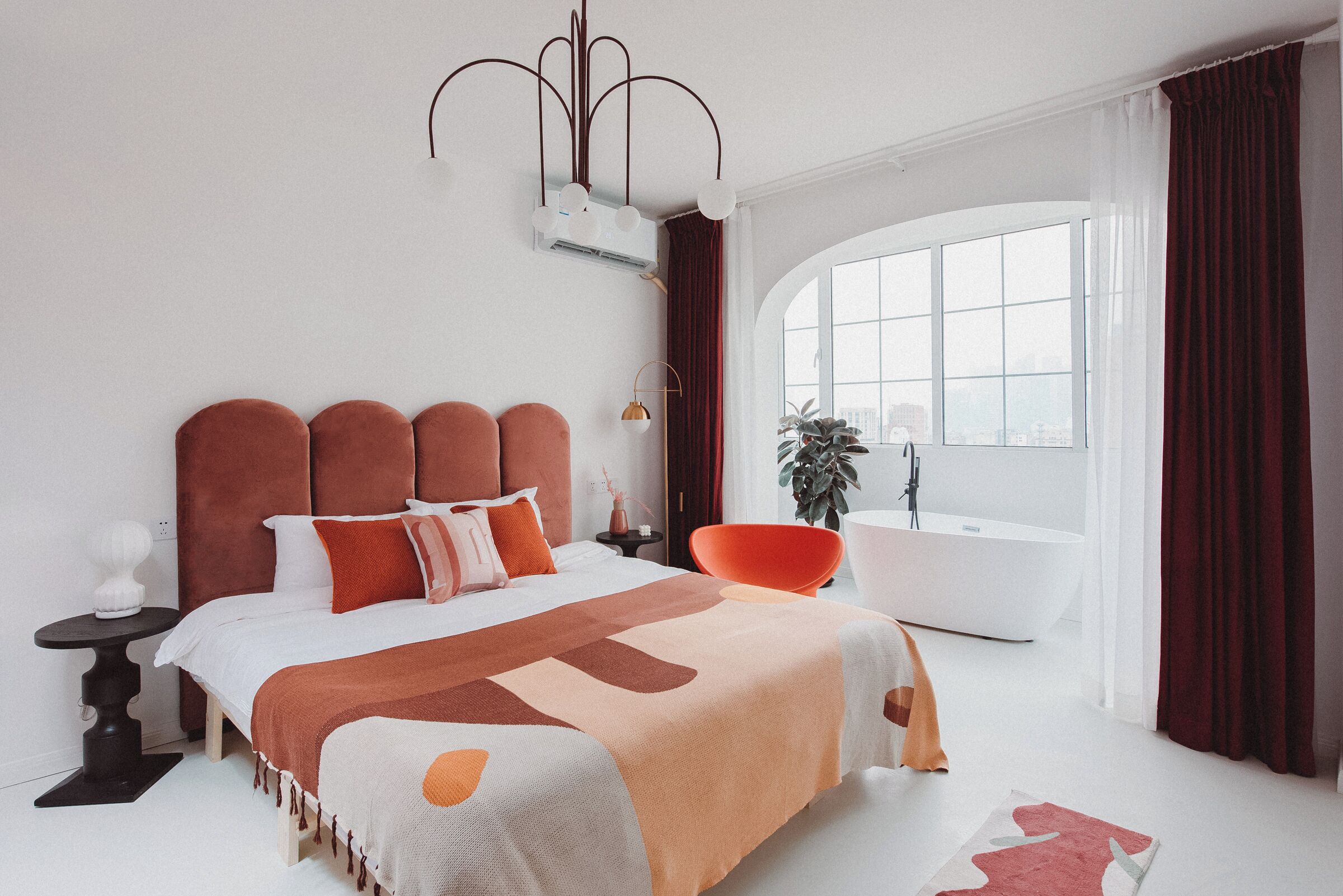 A modern bedroom with a large bed, a side table, a chair, a bathtub, and a window with curtains.