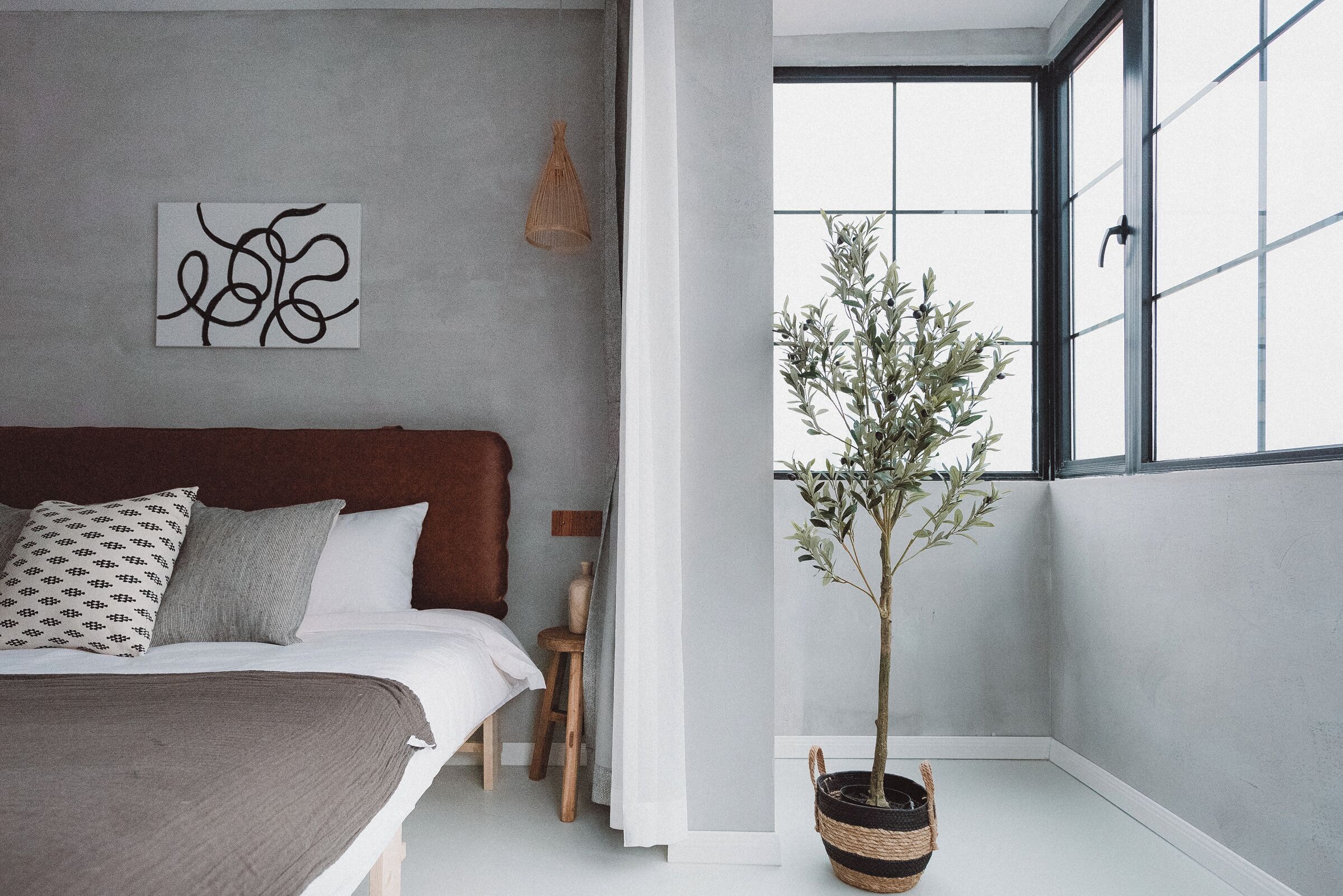 A bedroom with a bed, a wall art piece, a potted plant, and a window.