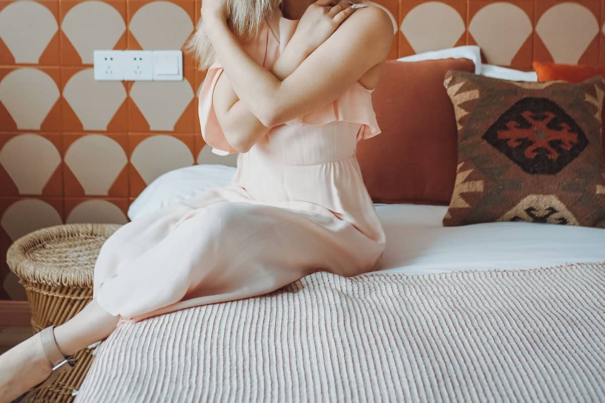 Una persona sentada en una cama frente a una pared estampada.