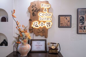 Een receptiebalie met een bord voor Pine & Cedar Suites, een ingelijst certificaat, een telefoon en een vaas met bloemen.