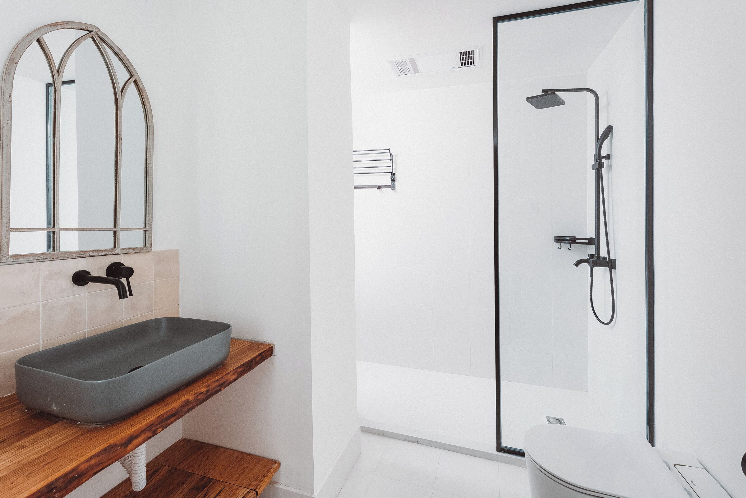 Ein Badezimmer mit einem rechteckigen Waschtisch, einem Holzregal, einem Spiegel, einer Duschkabine und einer Toilette.
