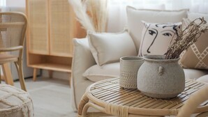 A cozy living room with a sofa, a wicker chair, a small table with a vase and a cup, and a cabinet with a plant. - Pine  Cedar Suites Hua Xiao Ye (Shanghai)