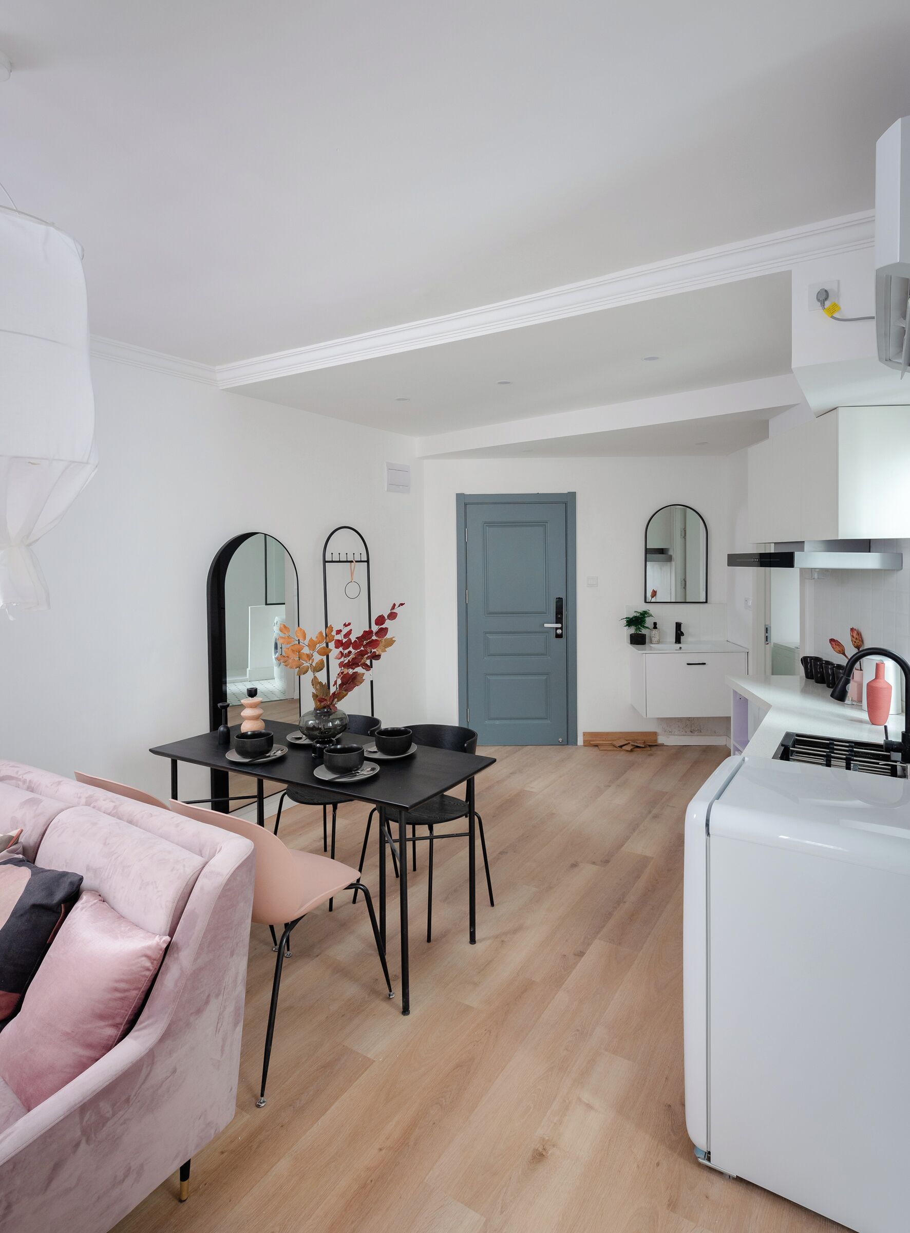 Une cuisine moderne avec des appareils électroménagers blancs, un coin repas avec une table et des chaises, et une porte bleue.