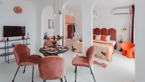 A modern hotel room with a TV, dining table, chairs, a bed with orange bedding, and a bathroom with a red chair. - Pine  Cedar Suites Hua Xiao Ye (Shanghai)