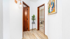 A hallway with wooden flooring, a potted plant, a wall-mounted light fixture, and a framed painting. - Apartment 'Madalena' with Private Pool, Wi-Fi and Air Conditioning (Carvoeiro)