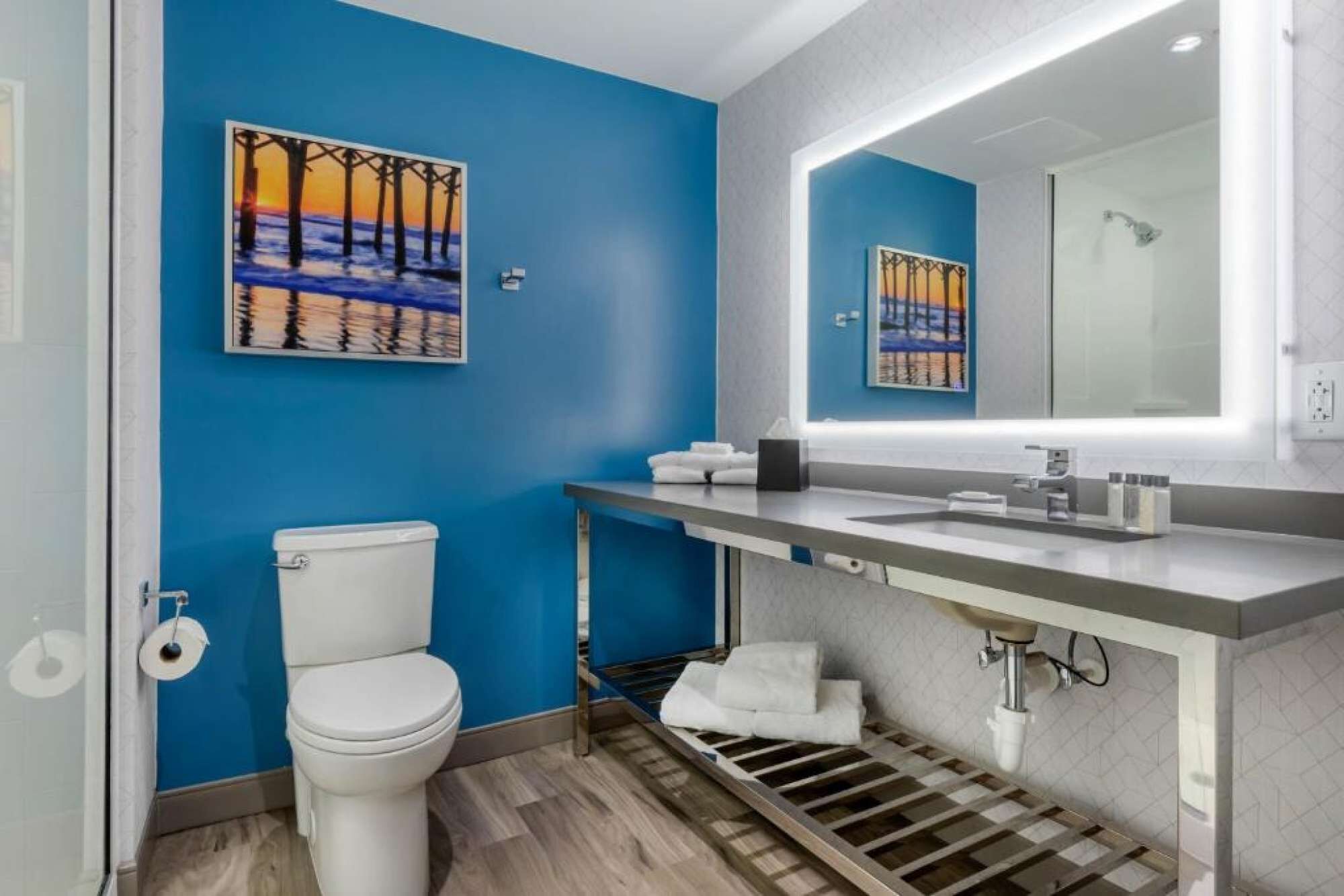 A bathroom with a blue wall, a white toilet, a sink with a mirror, and a shower.