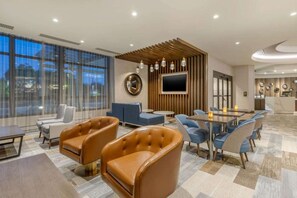 A modern hotel lobby with leather chairs, a TV, and a reception desk.