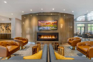 A modern lobby with a fireplace, leather sofas, and a large TV screen.