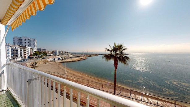 Een balkon met uitzicht op een strand, een palmpende en een jachthaven met boten.