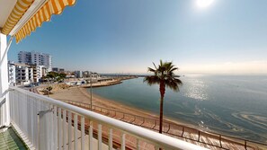 Un balcone con vista sulla spiaggia, una palma e un porto turistico con barche.