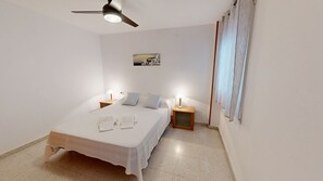 Une chambre à coucher avec un lit, deux tables de chevet avec des lampes, un ventilateur de plafond et un tableau accroché au mur.