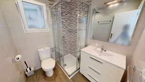 Een badkamer met toilet, een douche met glazen wand, een wastafel en een spiegel.