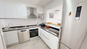 Een moderne keuken met witte kastjes, een roestvrijstalen koelkast, een magnetron, een fornuis en een vaatwasser.
