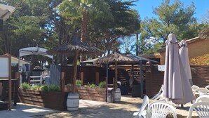 An outdoor patio area with thatched umbrellas, white plastic chairs, and a paved walkway. - LE COCON DE L'ARNEL (Villeneuve-lès-Maguelone)
