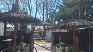 A pathway leading to a building with thatched-roof structures and wooden benches. - LE COCON DE L'ARNEL (Villeneuve-lès-Maguelone)