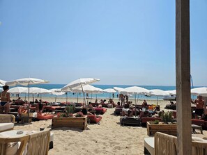Un paisaje playero con tumbonas, sombrillas y macetas de madera.