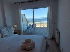 A bedroom with a bed, a nightstand, a lamp, a view of the beach, and a balcony with chairs. - Magnificent beachfront apartment with views of the sea and the port. (L'Escala)