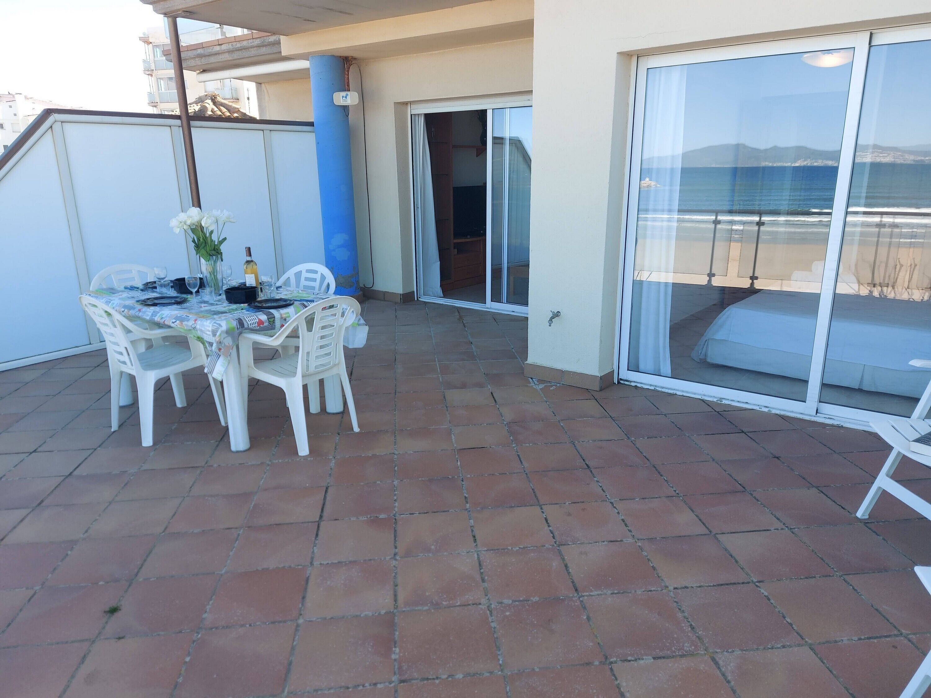 A patio with a table set for dining, a blue pillar, and a sliding glass door leading to a balcony.