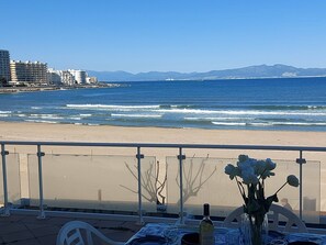 A seaside view with a table set for dining, a bottle of wine, and a vase of flowers. - Magnificent beachfront apartment with views of the sea and the port. (L'Escala)