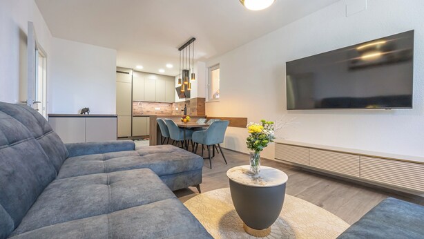 A modern living room with a sectional sofa, a round coffee table, and a flat-screen TV mounted on the wall. - Stylish apartment with terrace and private parking space in Crikvenica (Crikvenica)