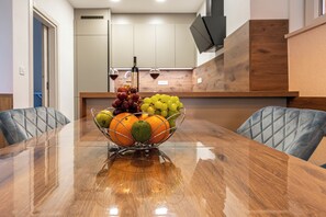 A wooden dining table with a fruit bowl in the center, two chairs, and a kitchen in the background. - Stylish apartment with terrace and private parking space in Crikvenica (Crikvenica)