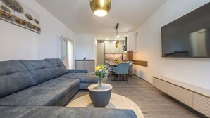 A modern living room with a sectional sofa, a round coffee table with a vase, a flat-screen TV, and a dining area in the background. - Stylish apartment with terrace and private parking space in Crikvenica (Crikvenica)
