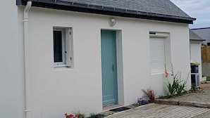 A single-story building with a dark roof, white walls, a green door, and a small window.