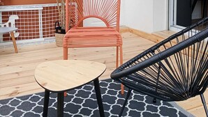 A patio with a round table, a red chair, a black chair, and a white door.