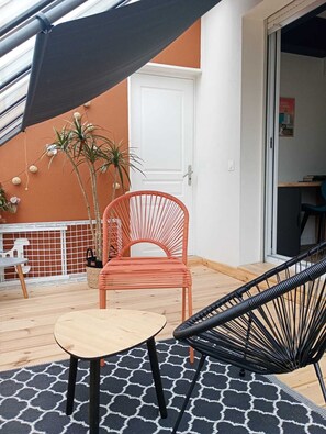 Un patio con una mesa redonda, una silla roja, una silla negra y una puerta blanca.