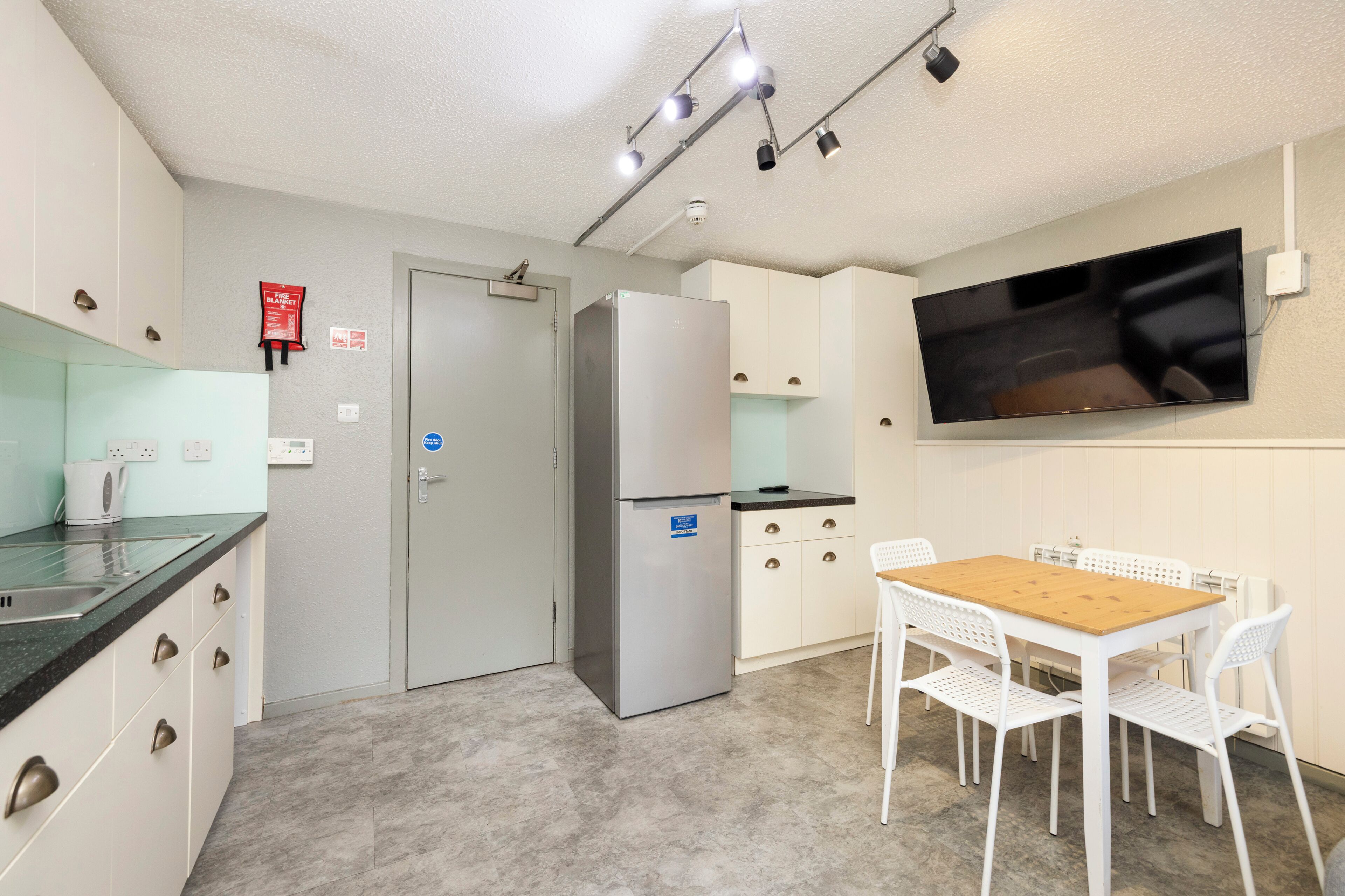 A compact kitchen with a refrigerator, a microwave, a sink, and a dining area with a table and chairs.