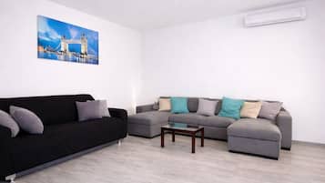 Una sala de estar con un sofá negro, un sofá seccional gris y una pequeña mesa de centro de madera.