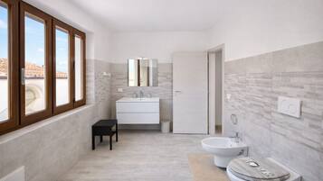 Un baño moderno con un ventanal grande, un lavamanos, un bidé y un inodoro.