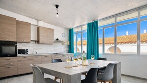 A modern kitchen with wooden cabinets, a dining table with chairs, and a view of the outside through large windows. - Bonòra suites (Tortolì)