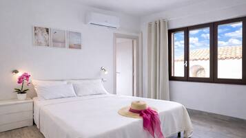 A bedroom with a bed, a nightstand, a potted orchid, a wall-mounted air conditioner, and a window with curtains.